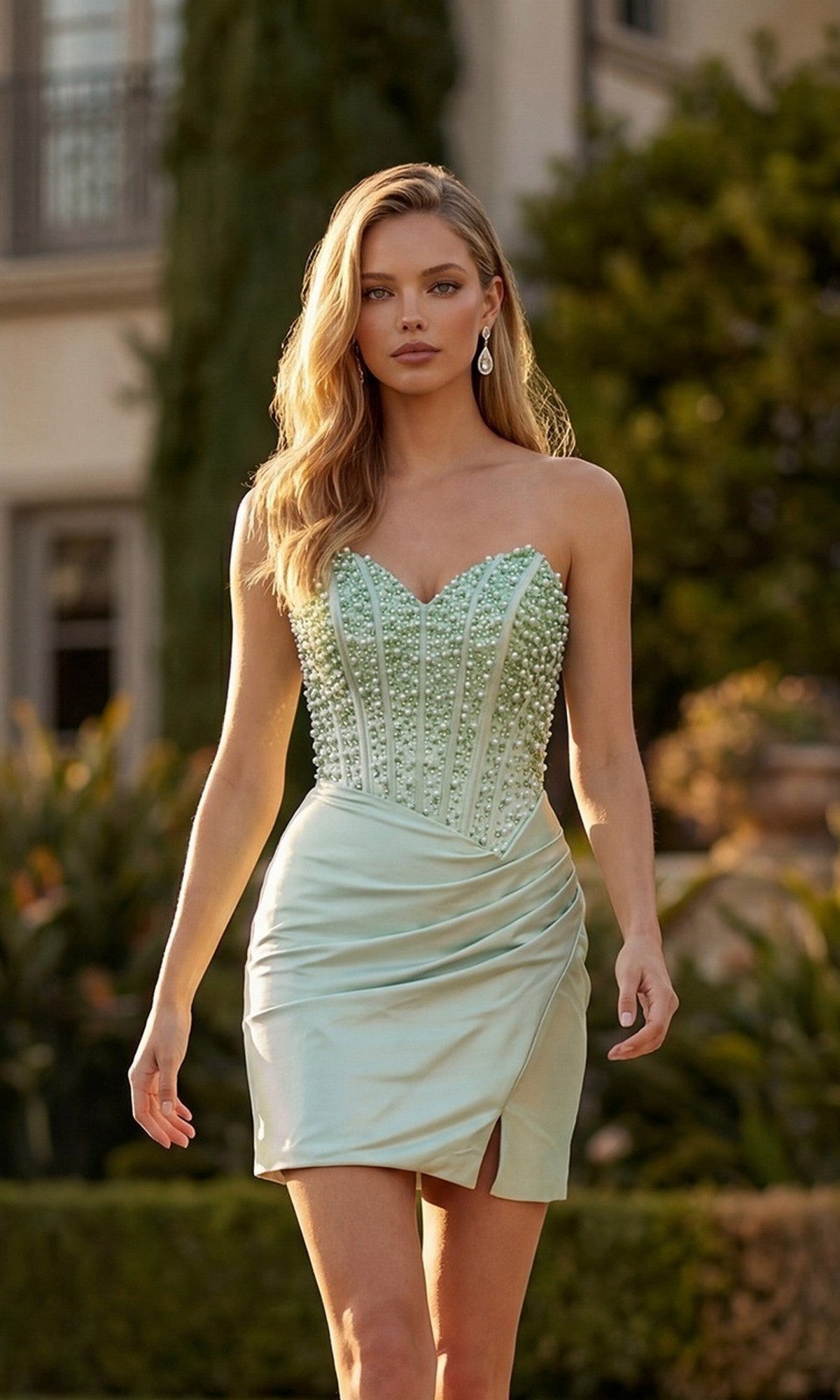 A woman walks outdoors in the Juliet JT7183U short homecoming dress, featuring a strapless beaded corset bodice and a wrap satin skirt in sage green.